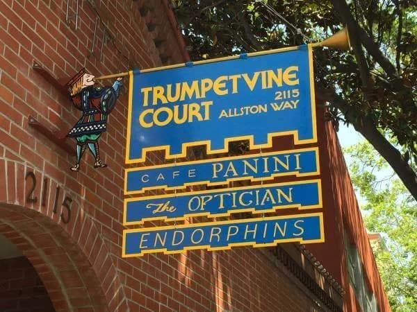 Blue and yellow projecting directory sign for Trumpetvine Court at 2115 Allston Way, listing Cafe Panini, The Optician, and Endorphins.
