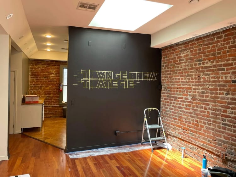 Masked layout guides for “Strange Brew Strategies” on a dark office wall beside exposed brick.