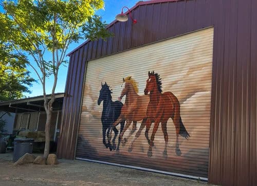 Muralist painting running horses across a residential wall