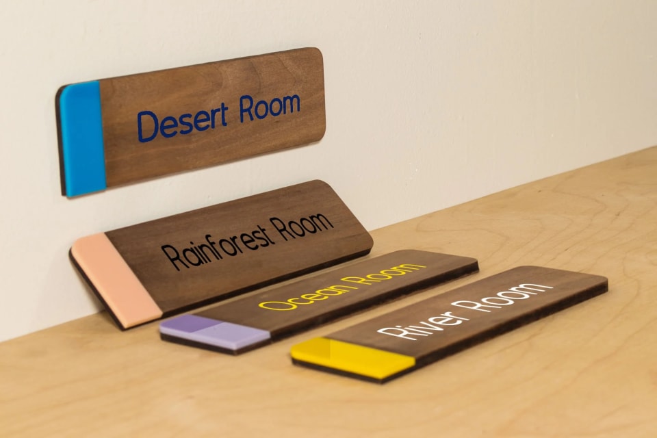 Several finished wood room placards arranged together on a work surface.