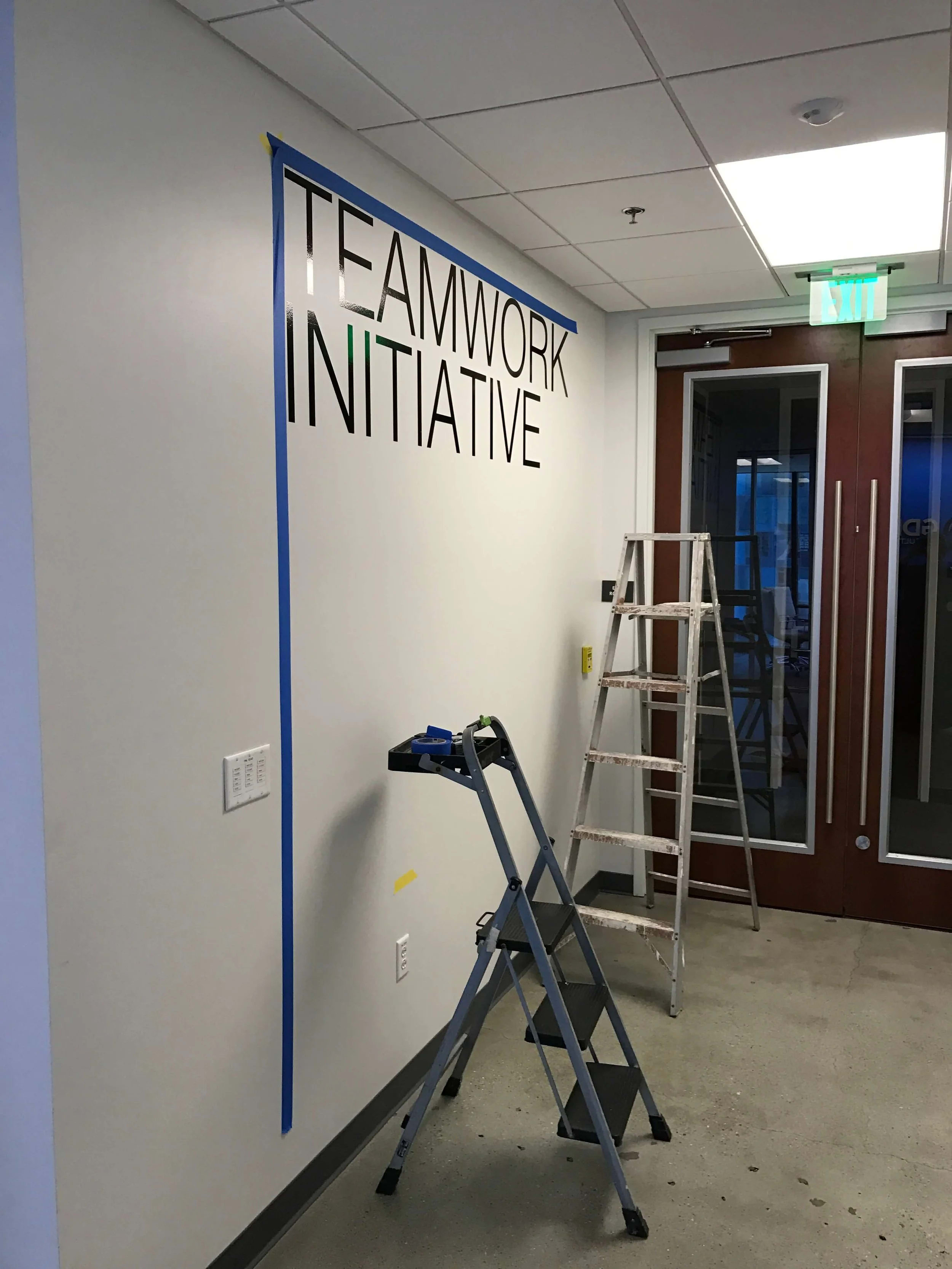 Black vinyl words being aligned within a taped layout on an office wall