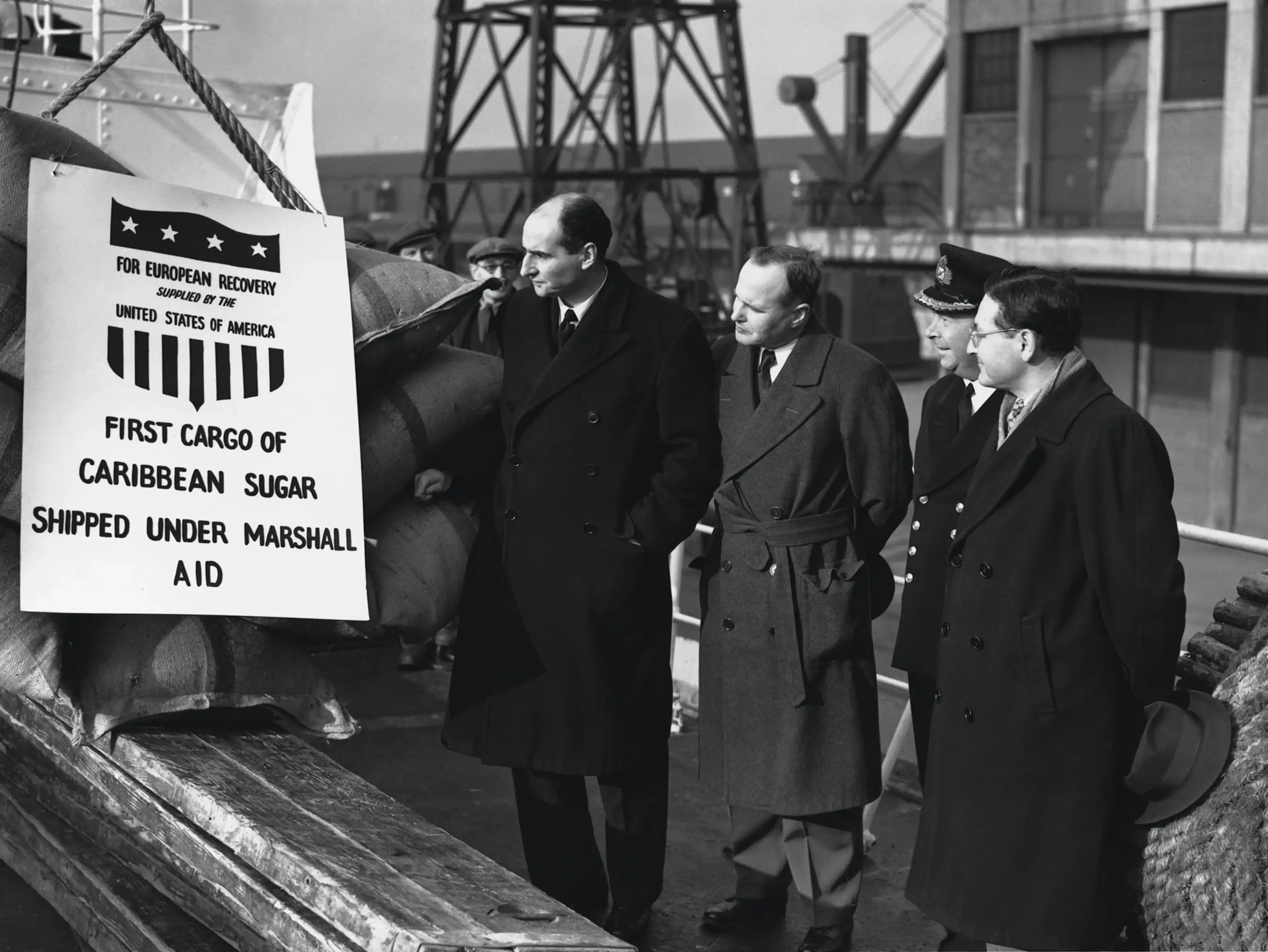 Officials inspect the first cargo of Caribbean sugar shipped under the Marshall Plan for European recovery, with a sign reading “For European Recovery Supplied by the United States of America,” circa 1948.