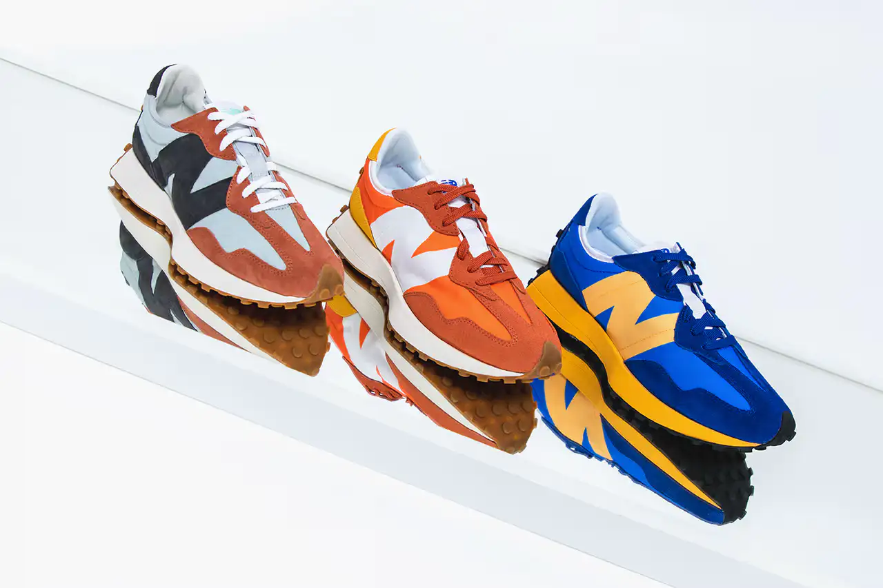 New Balance 327 sneakers in blue, orange, and red colorways displayed on reflective surface.