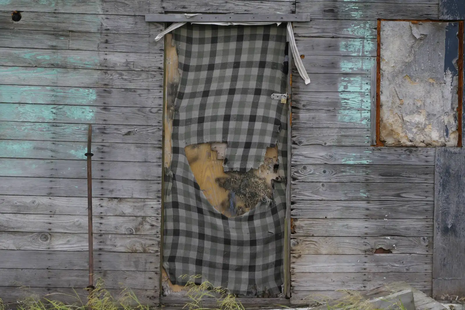 Weathered wooden wall of an abandoned house with a torn plaid cloth hanging over a doorway in Newtok, Alaska.