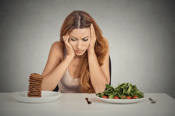 Woman sitting at a table, staring unhappily at a plate of plain vegetables.
