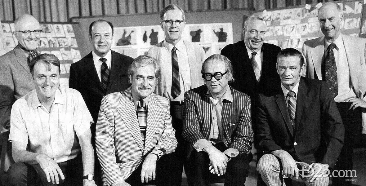 Black and white photo of Walt Disney’s Nine Old Men, the legendary team of animators who shaped Disney’s classic films, posing together in front of animation sketches.