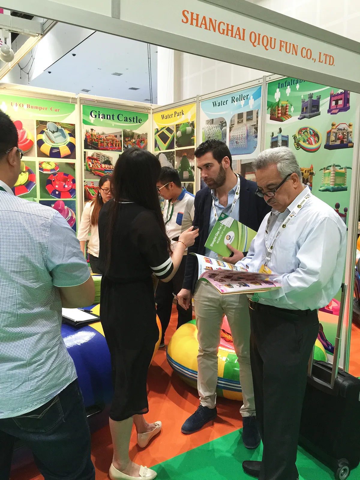Middle Eastern park operators deeply reviewing commercial amusement ride catalogs while Founder Emily handles parallel VIP inquiries at a packed IAAPA Dubai 2015 booth