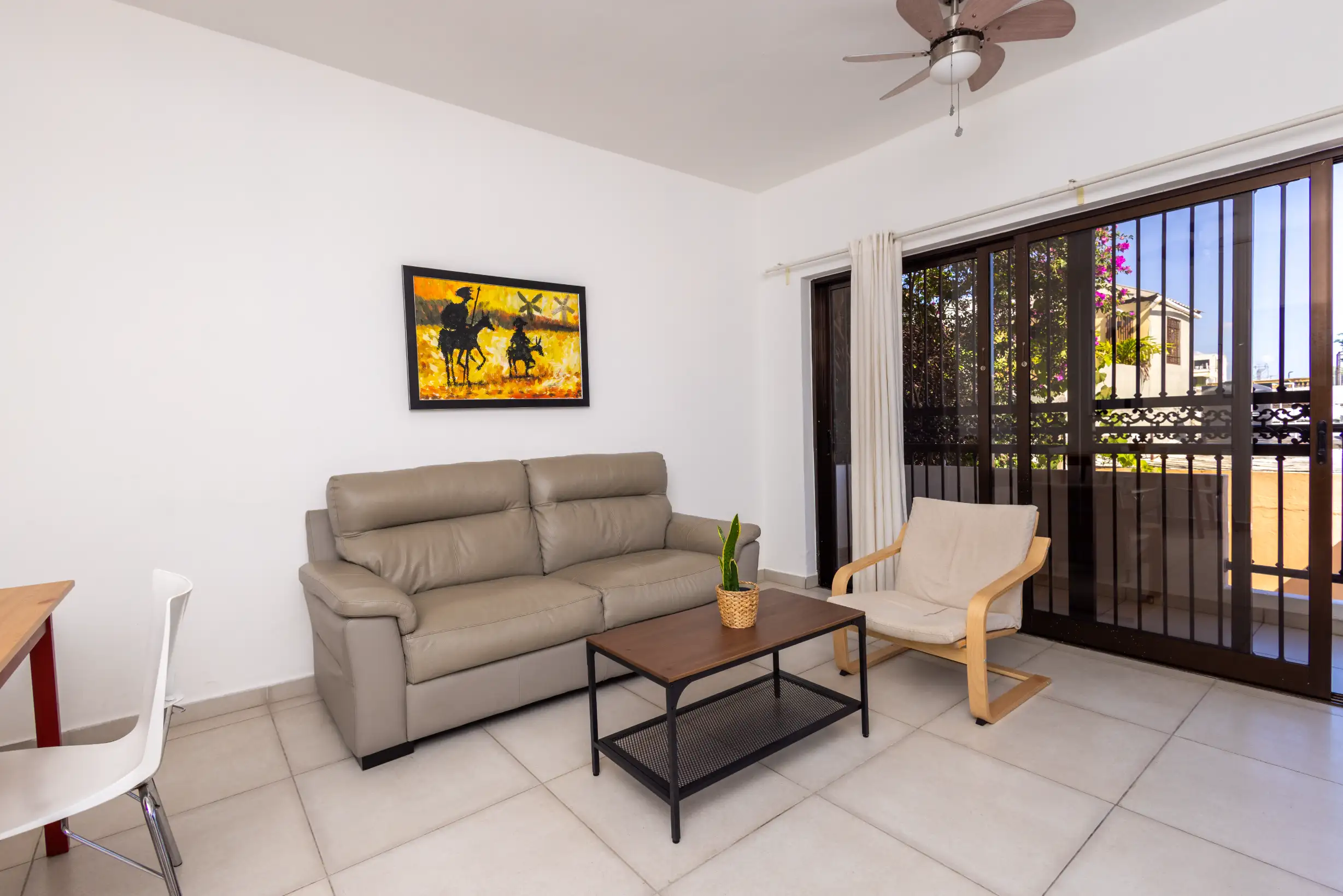 Living room with grey sofa, wooden armchair and Don Quixote artwork by the balcony — Unidad 1B