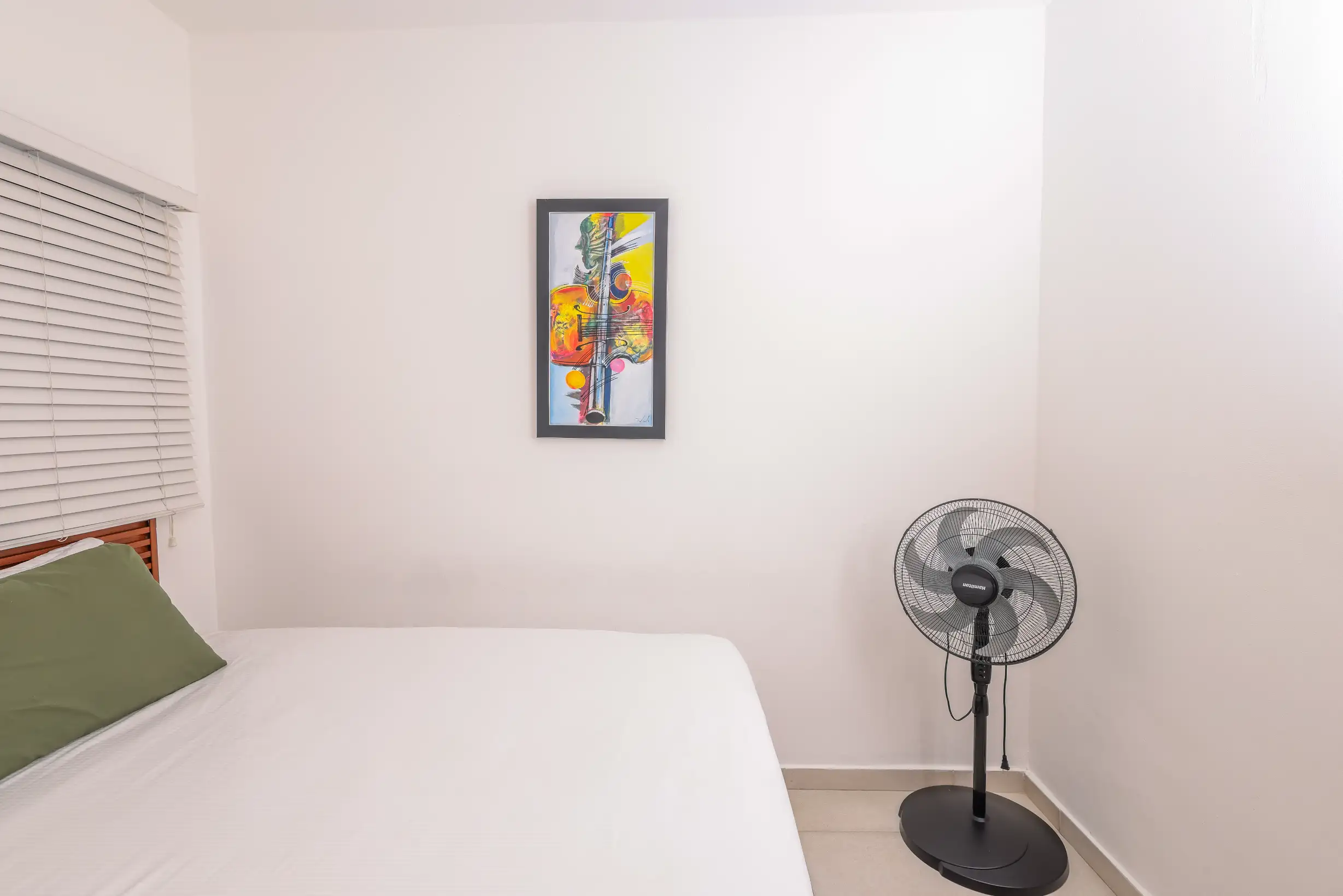 Bright bedroom with queen bed, standing fan and abstract artwork — Unidad 3B
