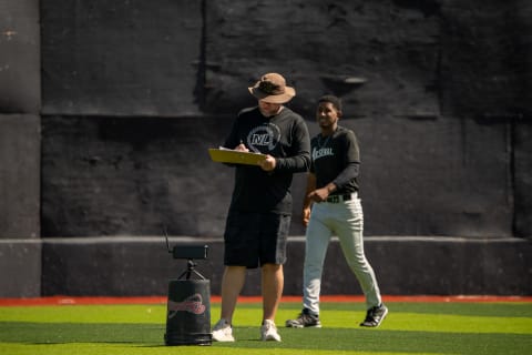 A coach with a clipboard evaluating a player, with a radar unit set up on the field
