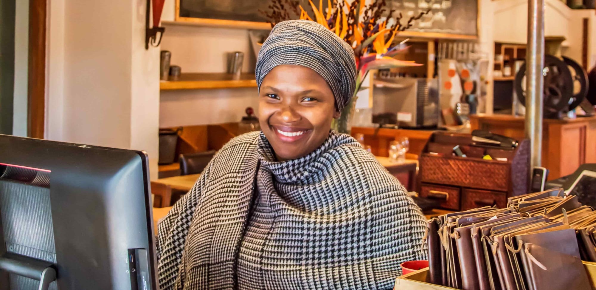 A friendly cashier wearing traditional attire behind the counter of a cozy, rustic cafe.