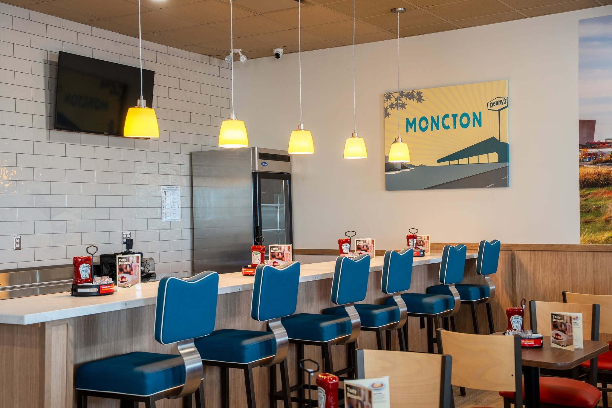 Interior of the new Denny's in Moncton, NB — counter with pendant lights, red booths and the Denny's sign, photographed before opening