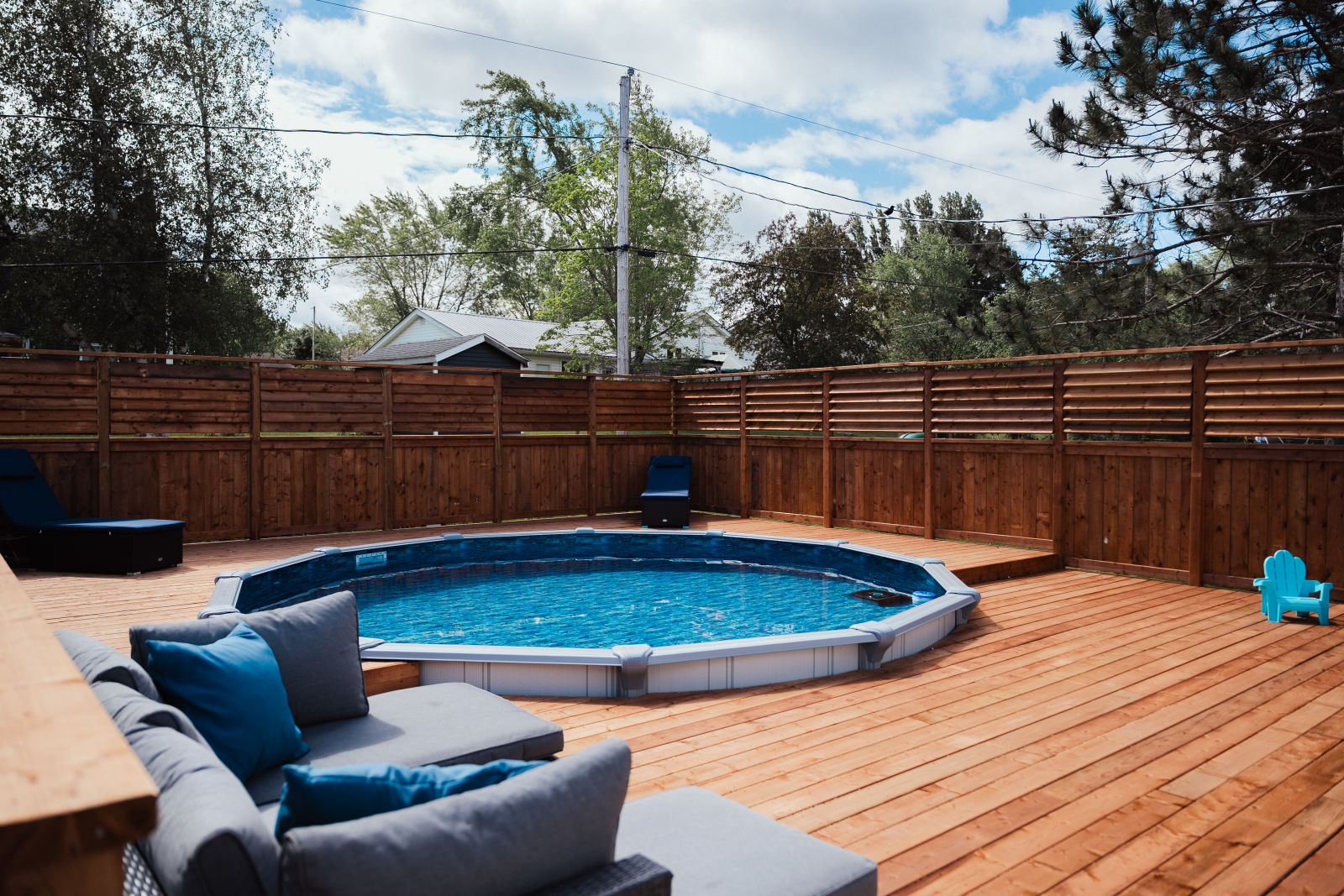 Ground-level view of a wraparound pool deck in Riverview NB with horizontal-louver privacy fence and a built-in lounge sectional