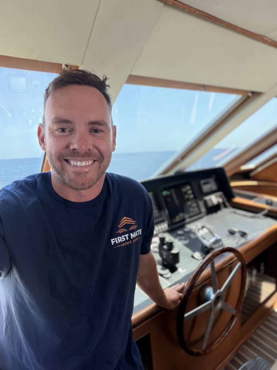 Luke Ludemann of First Mate Yacht Club at the chart table aboard a yacht in San Diego, helm wheel behind him