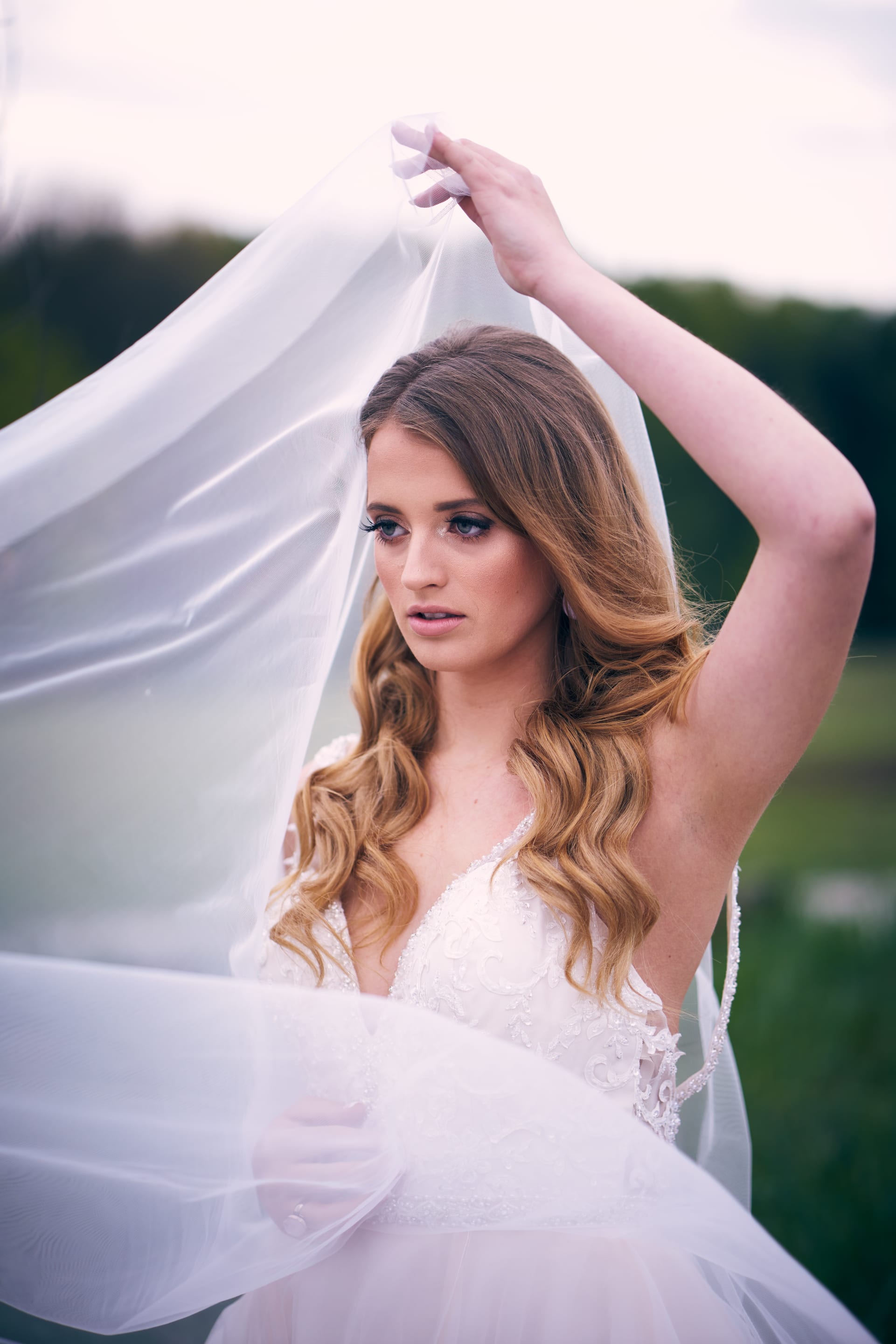 A woman in a white dress poses with a veil. The shot focuses on her face and the textures of the fabric and dress.