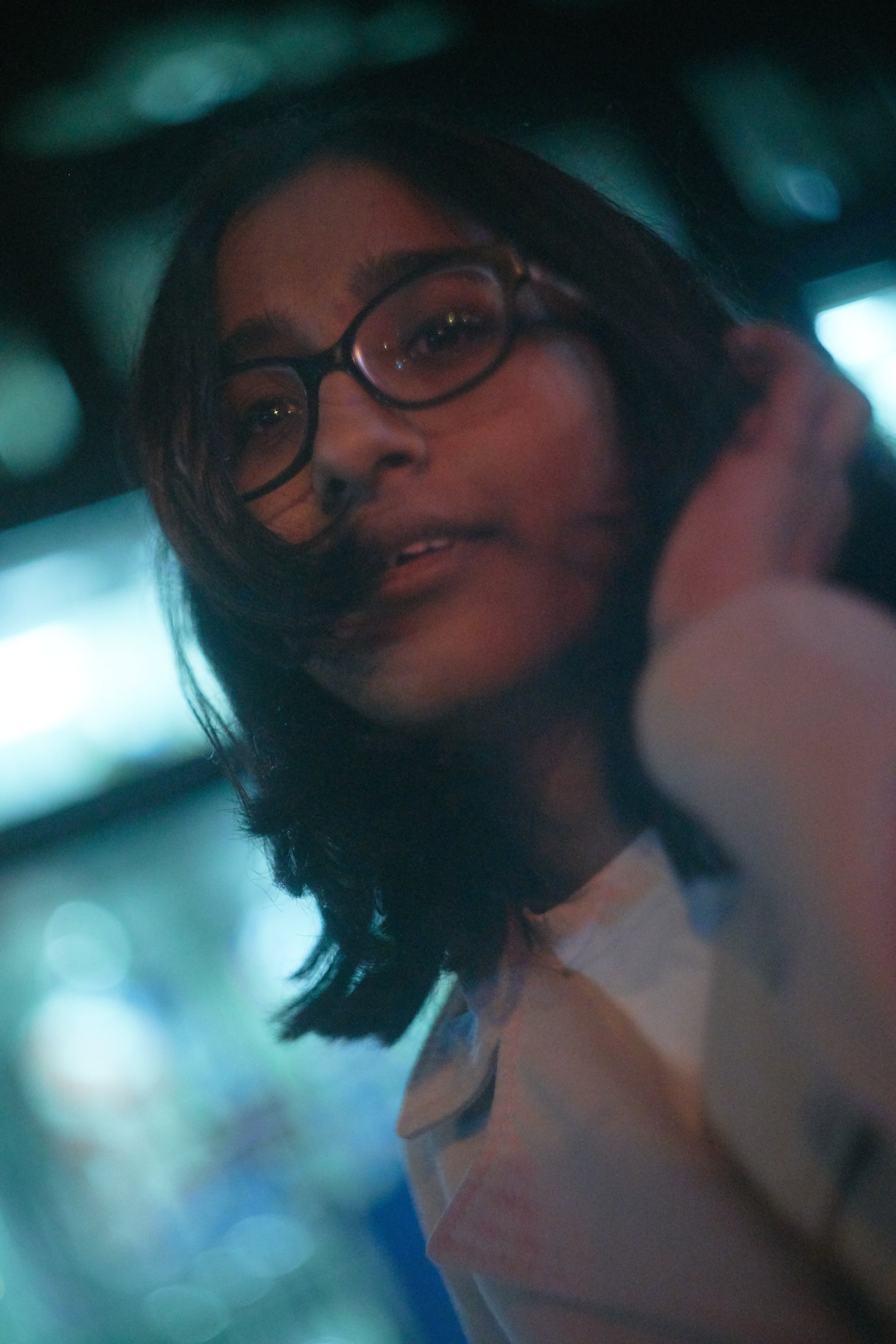 A portrait of a young woman with glasses, captured in a soft and intimate style. The background is blurred, with cool tones adding depth.