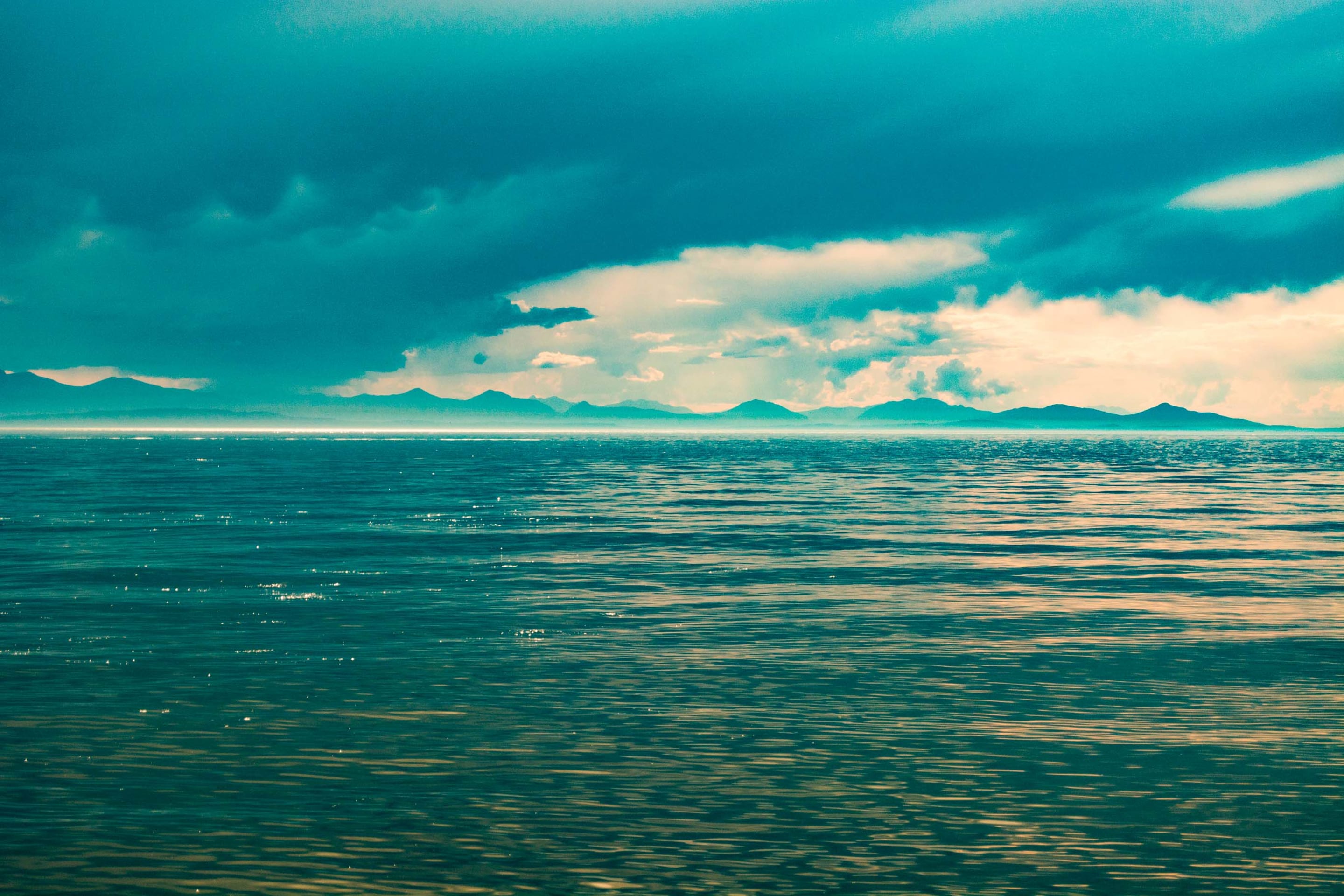 A serene landscape featuring a calm body of water beneath a cloudy sky, with distant mountains adding depth.
