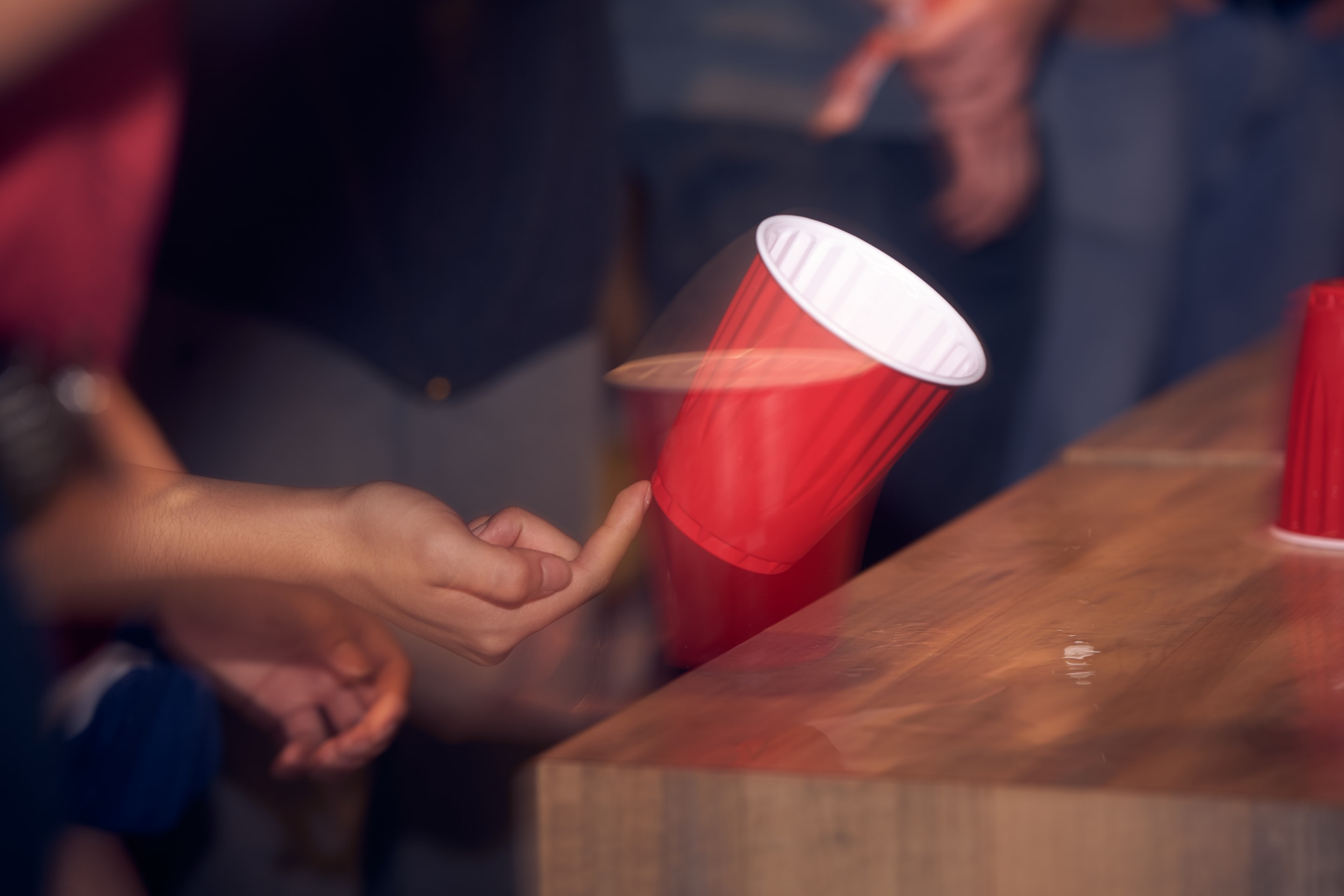 An image capturing a moment of a red cup being flipped in the air, likely during a game or celebration. The image captures a sense of movement and dynamism.
