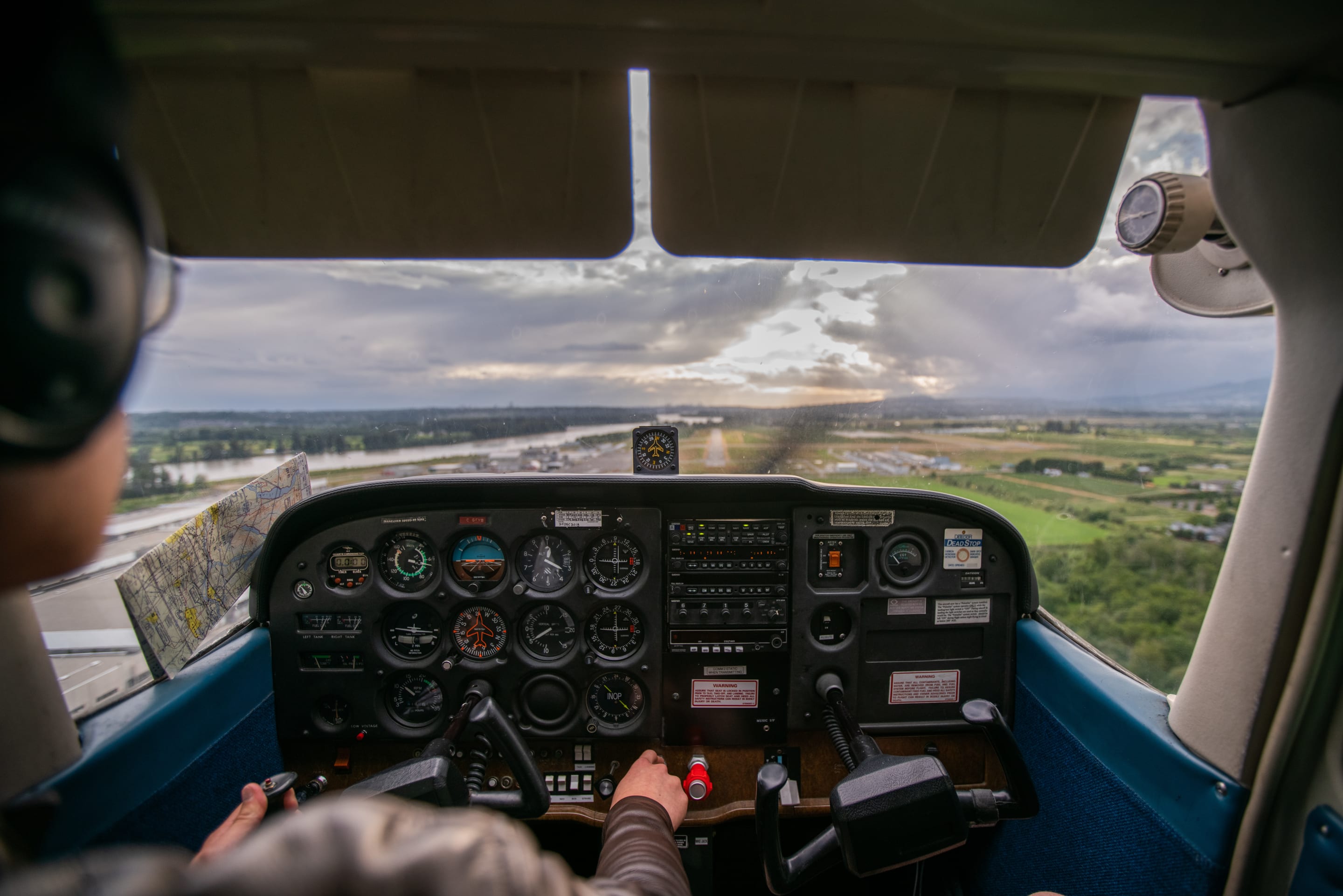 An interior view of a small airplane cockpit with a pilot at the controls, looking out over a scenic landscape.
