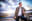 A man leans against an airplane wing, gazing off into the distance. The sky is filled with beautiful clouds and sunset. blurred out low res