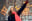 A woman joyfully points upwards while it snows. The background features bokeh lights, enhancing the festive atmosphere. blurred out low res
