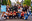 A group of young adults poses for a photo at an amusement park. Most of them are wearing face masks, and holding a sign that says "Group 16 Science Frosh." blurred out low res