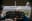 An interior view of a small airplane cockpit with a pilot at the controls, looking out over a scenic landscape. blurred out low res