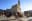 A low-angle shot captures pigeons in the foreground, with a historic building and clear blue sky in the background. blurred out low res