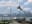 The image captures a scenic view of Toronto's skyline with several seagulls in the foreground. The CN Tower is prominently featured against a backdrop of a cloudy sky. blurred out low res