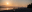 A tranquil scene of a beach at sunset, with the sun setting over the mountains and a city skyline in the distance. blurred out low res