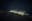 A nighttime landscape shows a mountain range with illuminated slopes and a cloudy sky. The scene is illuminated by lights scattered across the mountain. blurred out low res