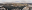 An aerial panoramic view of a city skyline on a cloudy day. The city has tall buildings and is situated near a body of water with boats. blurred out low res