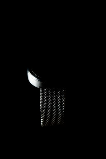 A close-up photograph showcasing a silver object with a mesh band, set against a stark black background.