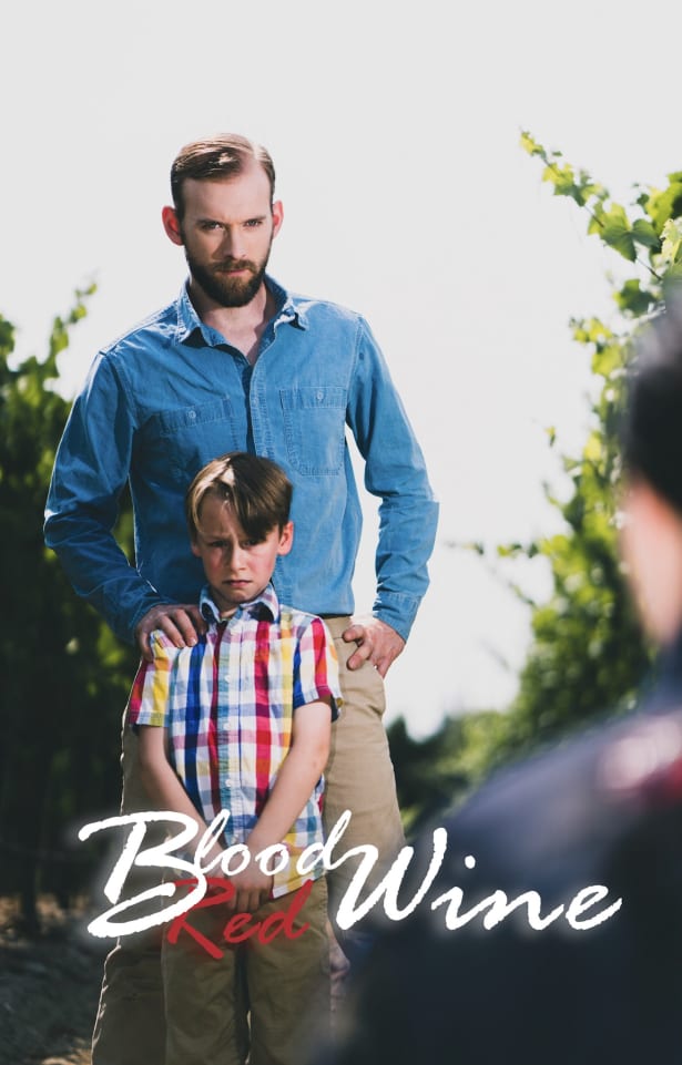 An adult and a child stand in a vineyard, with the child looking upset. The image has text overlaid that says 'Blood Wine Red'.