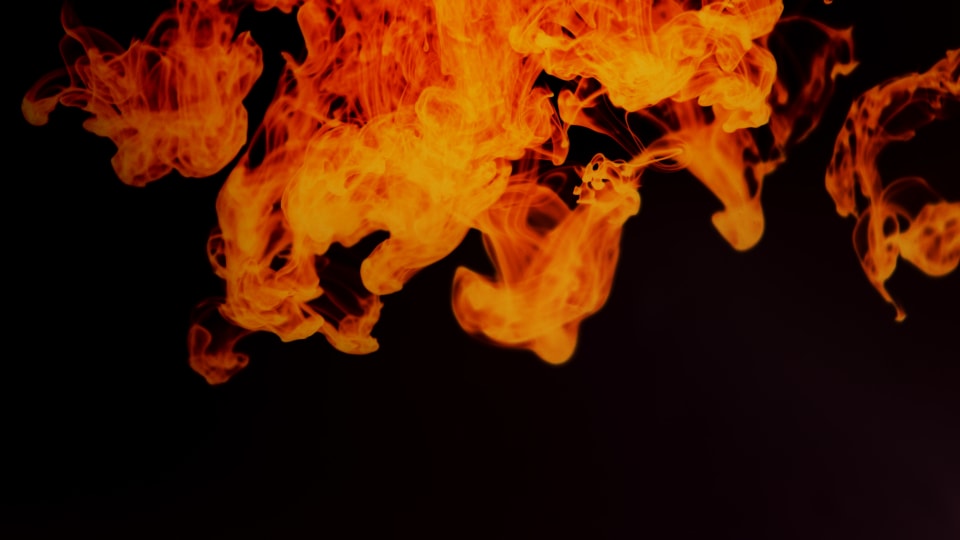 Abstract image of orange, swirling, smoke-like forms set against a black background. The forms evoke a sense of movement and energy.