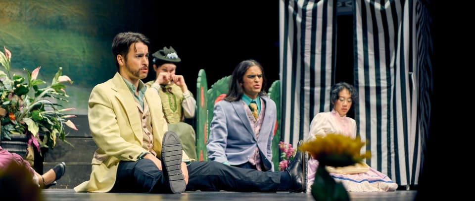 This image captures a stage performance with several actors in period costumes. The composition highlights a moment of drama during the play.