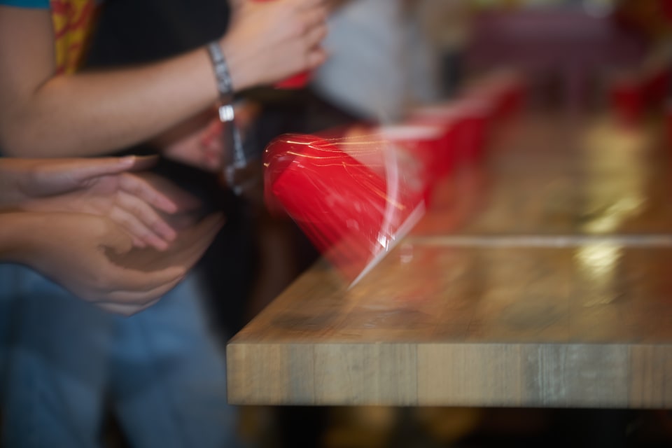 The image features a blurred composition of hands, red objects, and a wooden surface. The focus is on the motion and interaction within the scene.