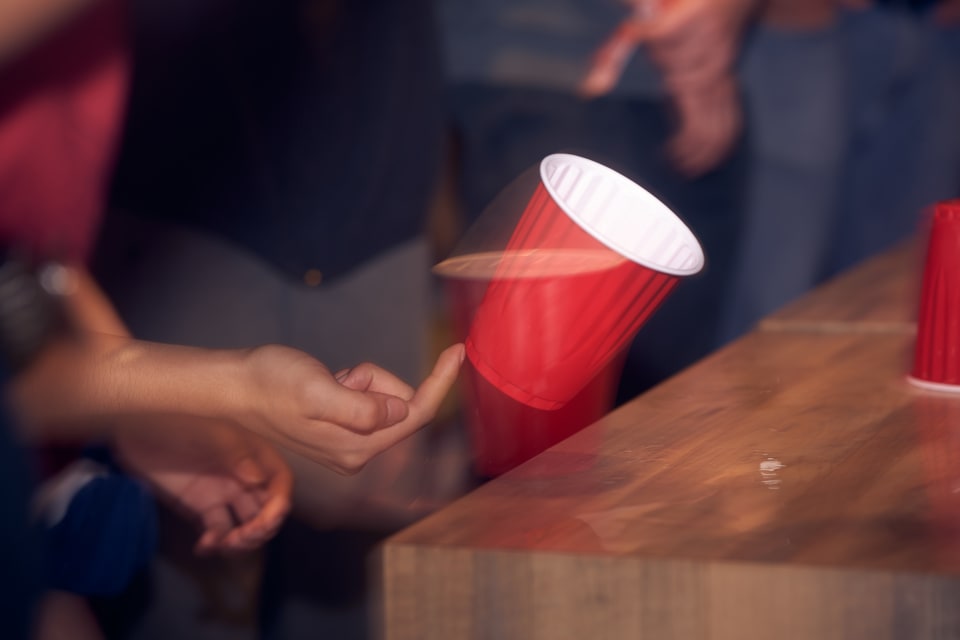An image capturing a moment of a red cup being flipped in the air, likely during a game or celebration. The image captures a sense of movement and dynamism.