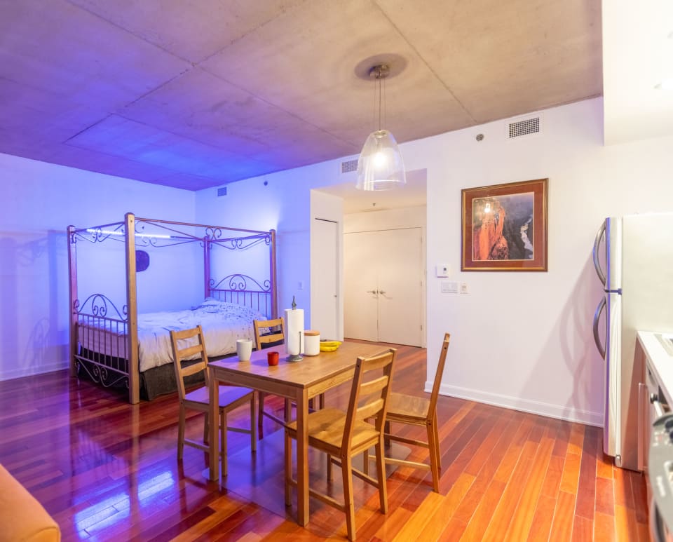 A modern living space with a canopy bed and dining table. The image showcases a minimalist interior with hardwood floors and ambient lighting.