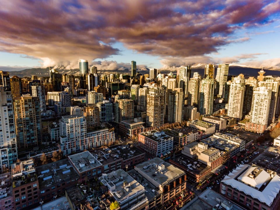 An aerial view of a cityscape with a dramatic sky. The image captures a bustling urban environment bathed in the warm light of sunset.