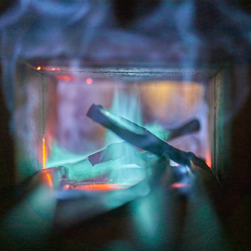 The image captures a close-up of a burning fire, with vibrant blue and orange flames illuminating wooden logs within a confined space.