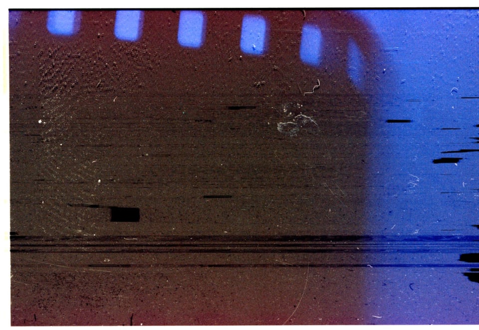 This abstract image displays the texture and imperfections of old film  stock, featuring a gradient from dark, reddish-brown to vibrant blue,  interspersed with scratches and dust.