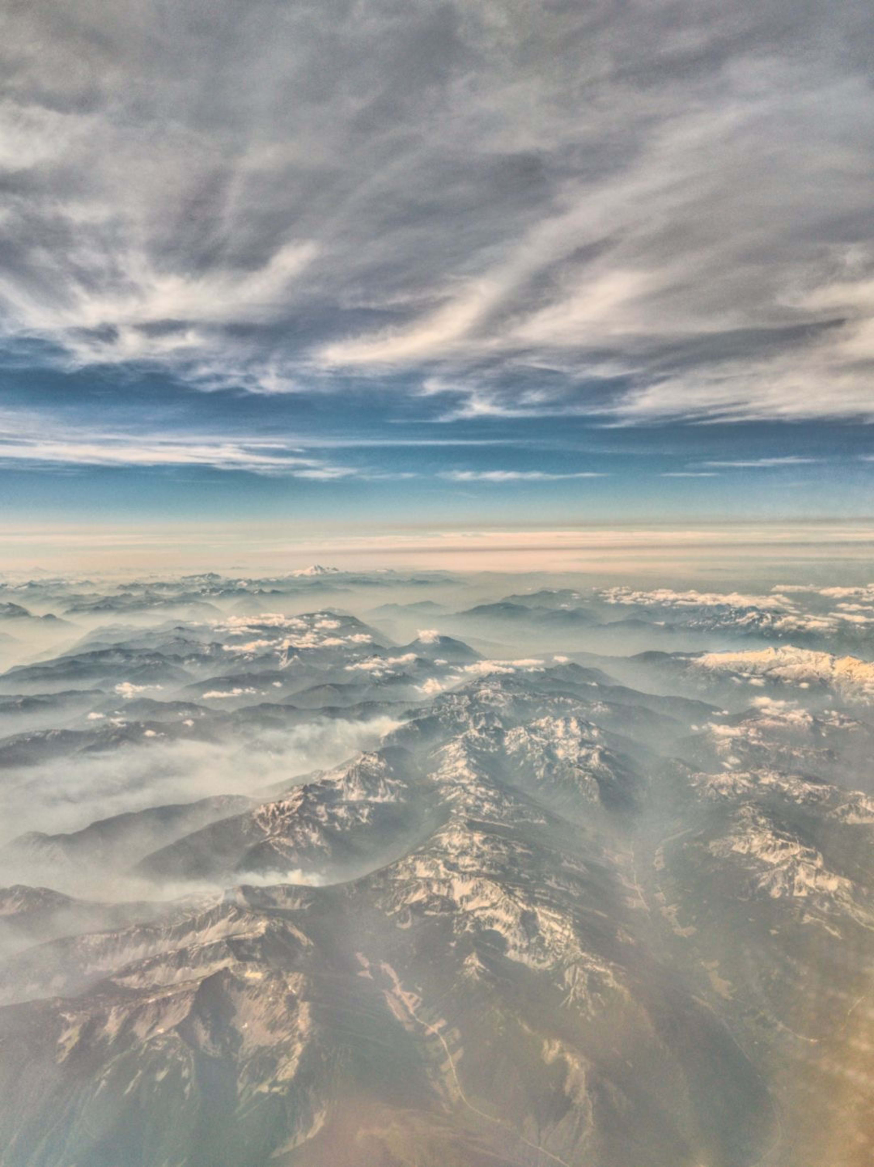 Snow-covered mountains and mist seen from above under a cloudy sky.