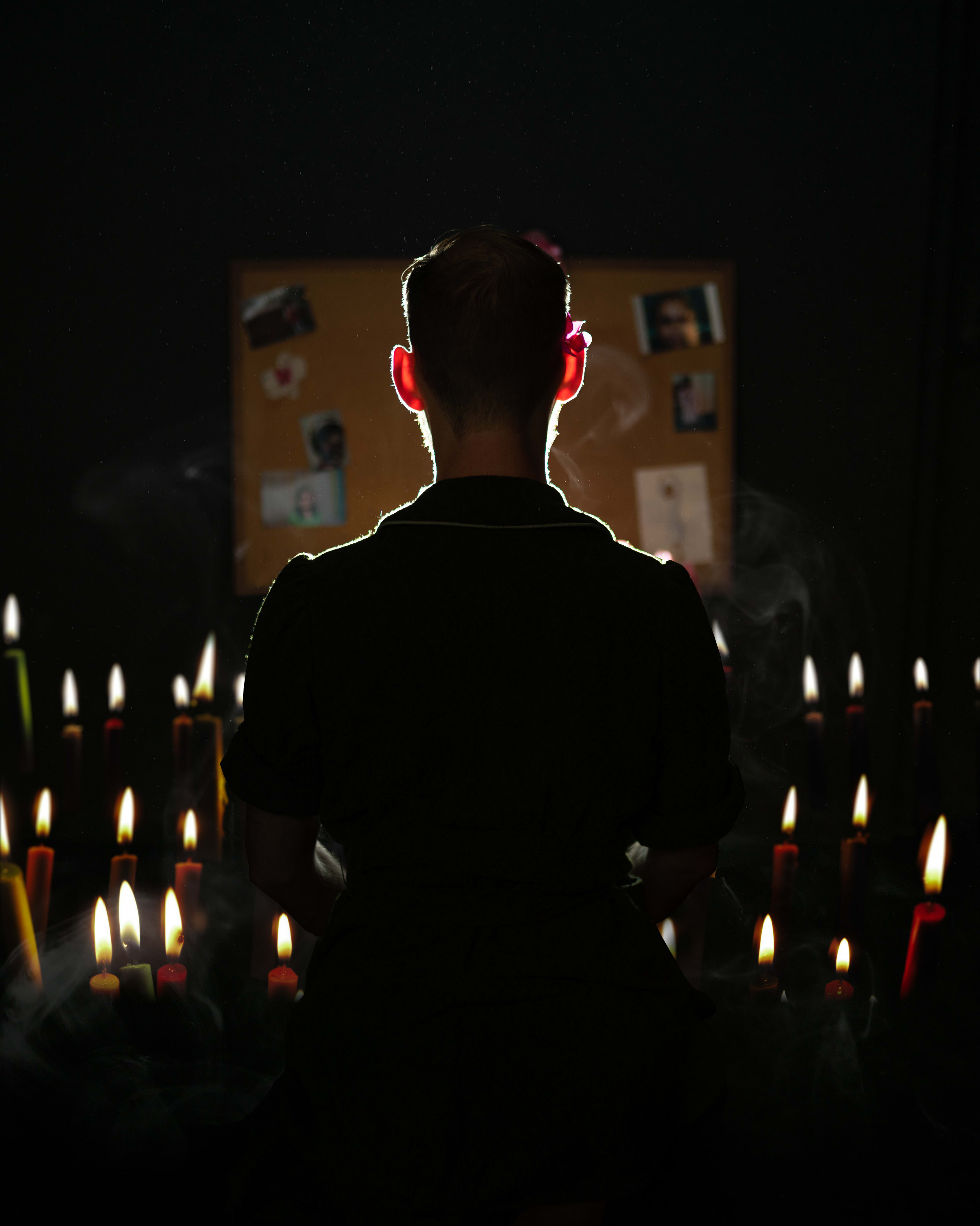 A figure stands in front of photos and candles.