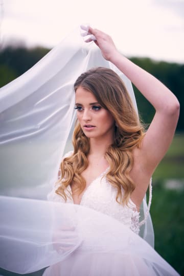 A woman in a white dress poses with a veil. The shot focuses on her face and the textures of the fabric and dress.