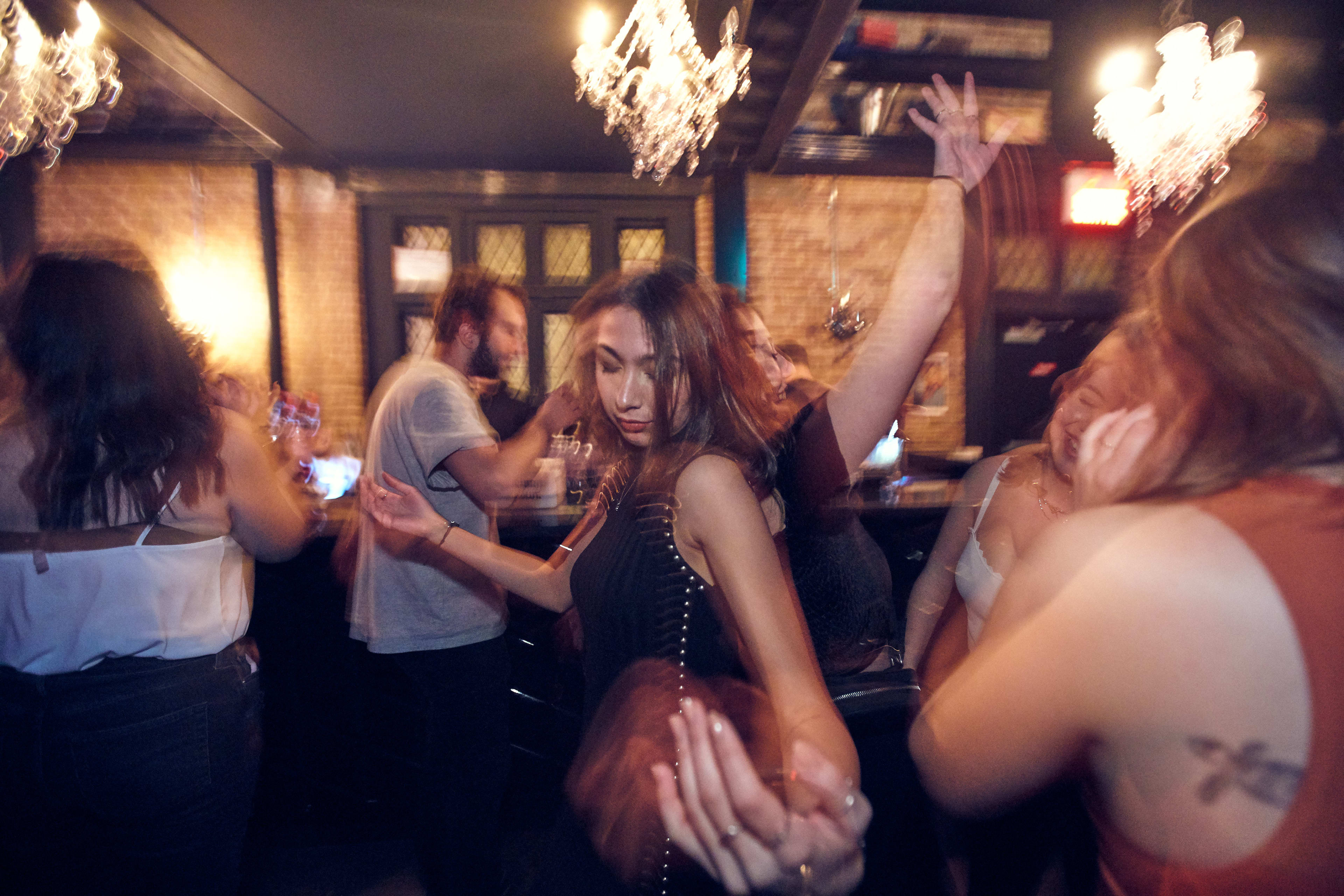 The image captures a lively dance scene in a dimly lit space.  People are blurred with motion, illuminated by the warm glow of chandeliers and ambient light.