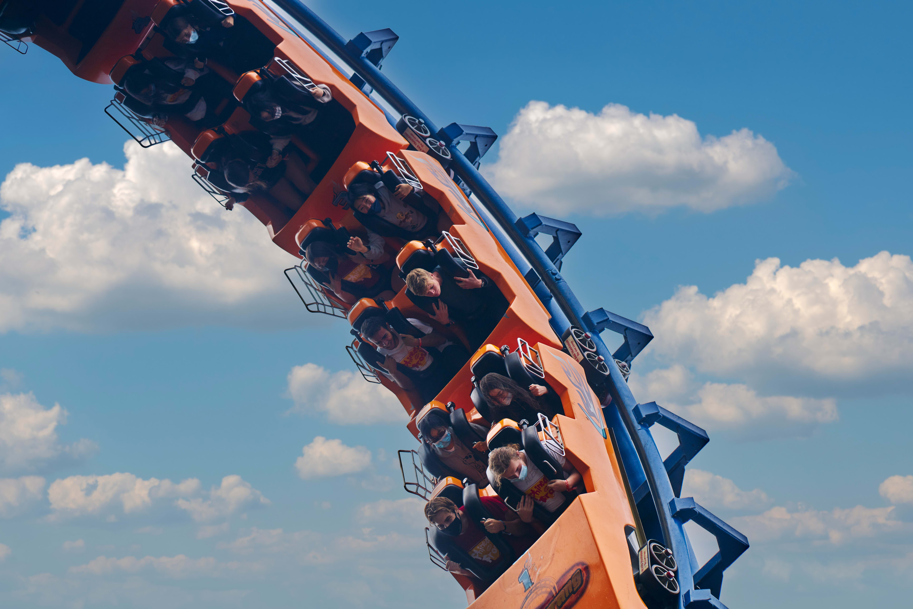 A roller coaster car climbs the track against blue sky and white clouds.