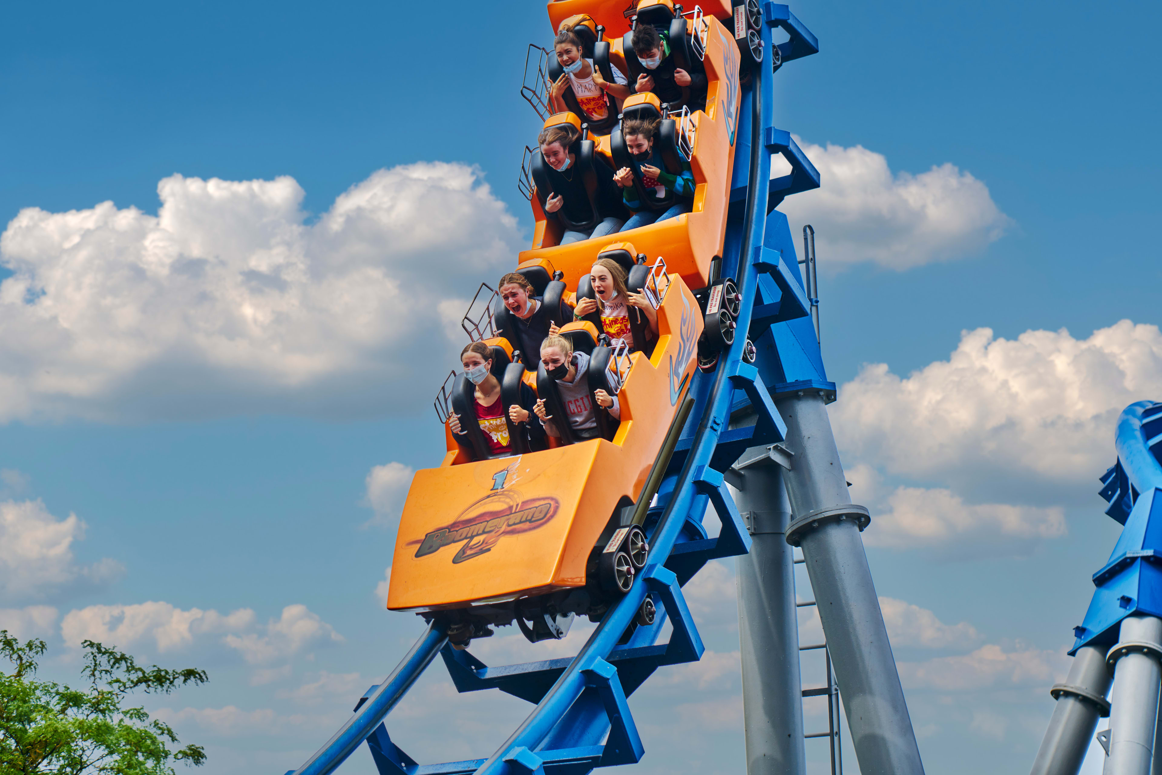 Passengers crest a roller coaster track against a bright blue sky.