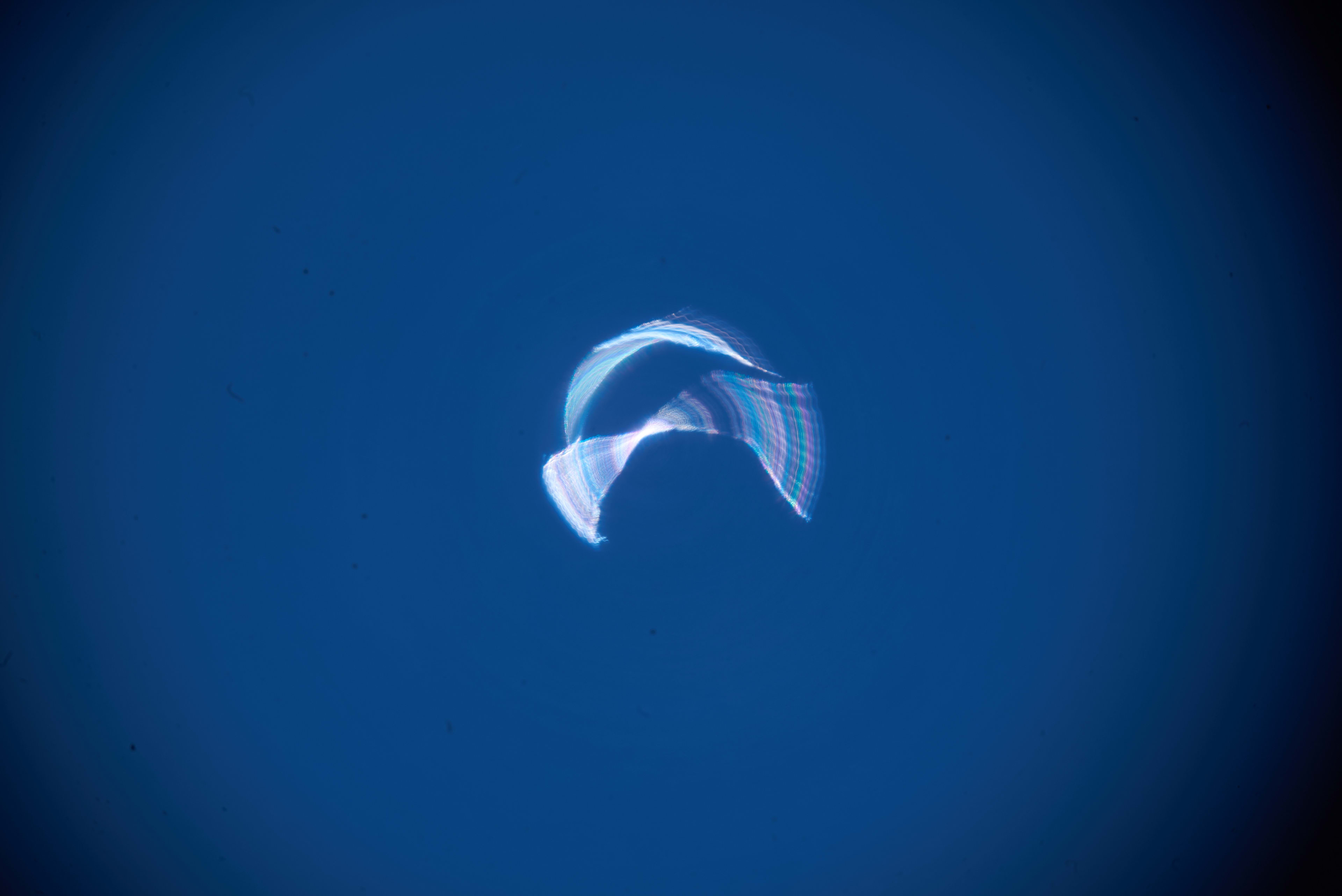 A pale blue and purple ribbon of light crosses a dark blue field.