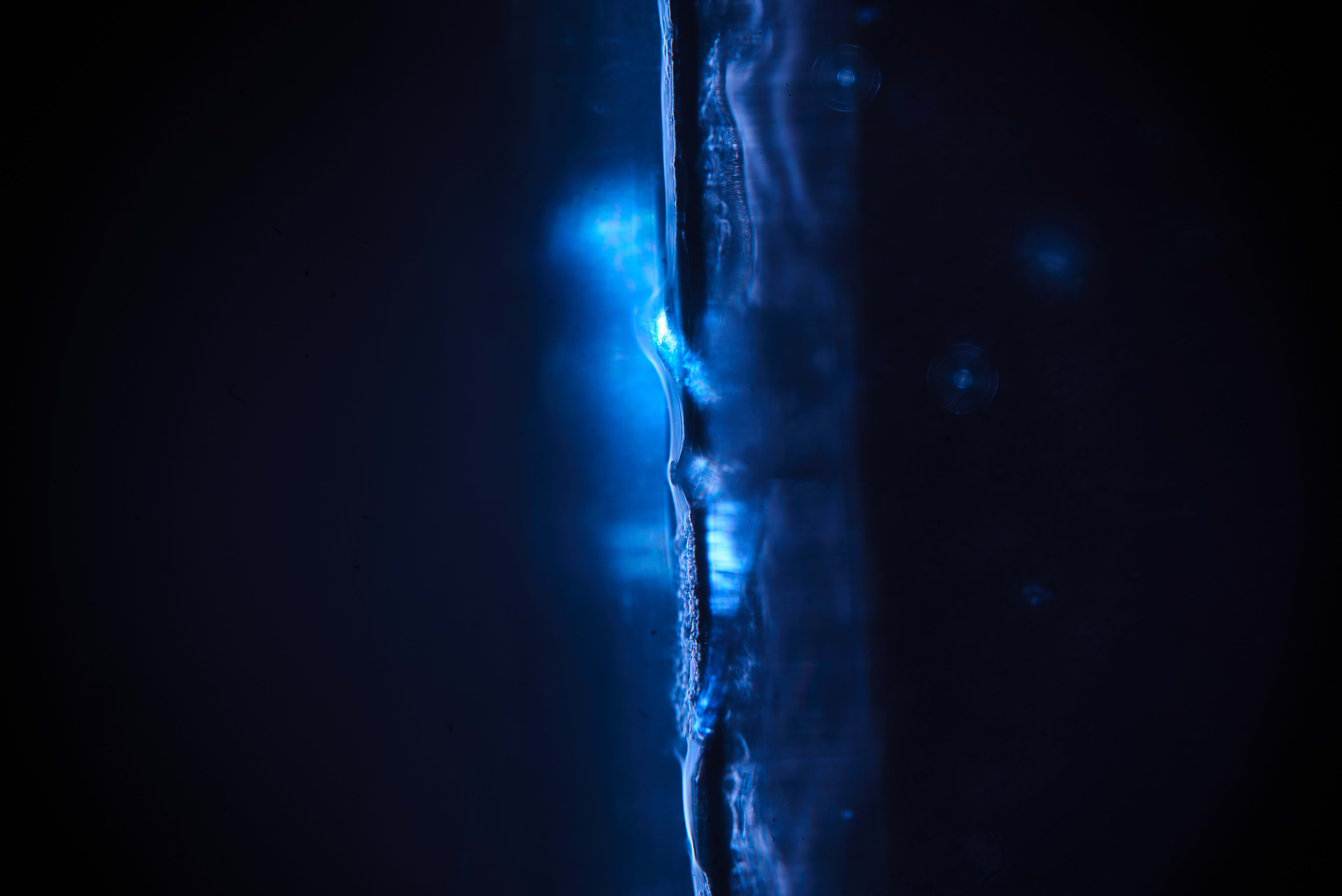 Dark blue liquid runs down a textured surface, catching small lines of light.